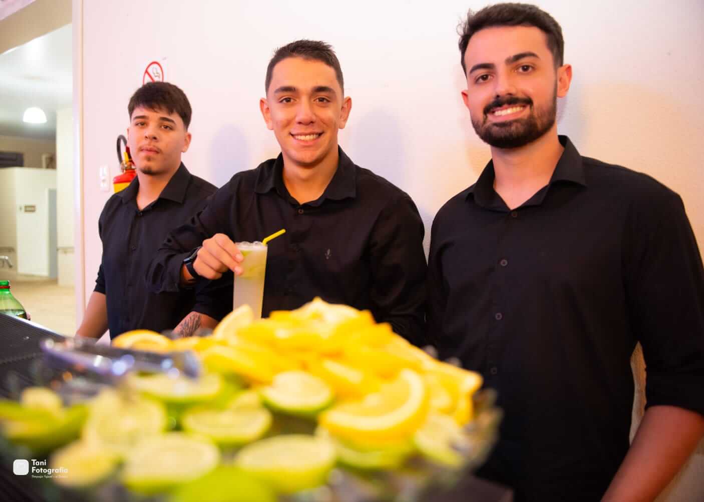 Equipe do G10 Drinks sorrindo atrás do balcão, com limões fatiados em primeiro plano